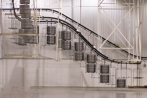 Monorail overhead conveyor moving cylindrical components along an elevated track