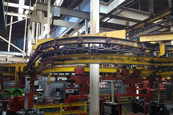 Monorail overhead conveyor moving cylindrical components along an elevated track