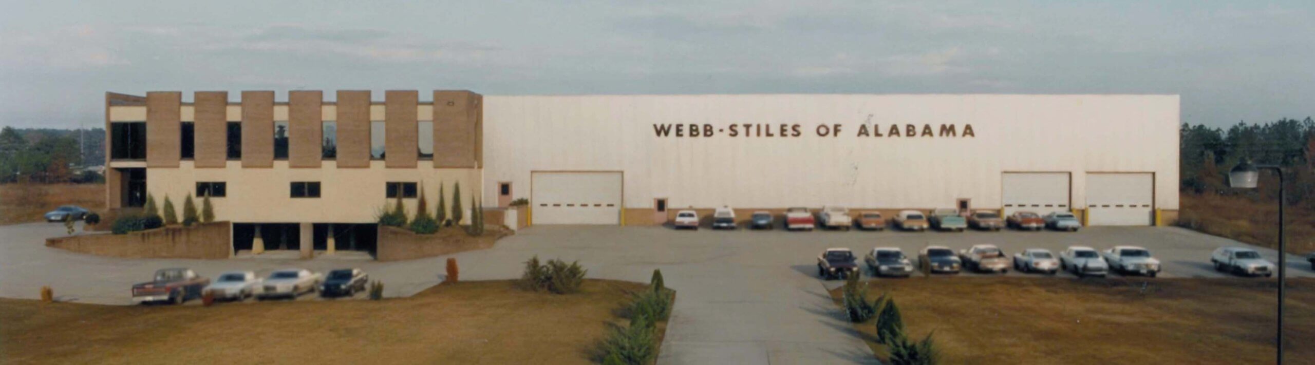 Exterior view of the Webb-Stiles of Alabama manufacturing plant, showing the office building and main facility with parked vehicles in front.