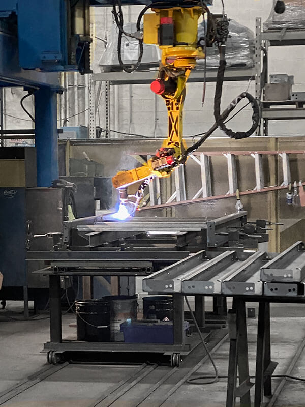 Gantry-mounted robotic welder operating on a steel conveyor frame at Webb-Stiles