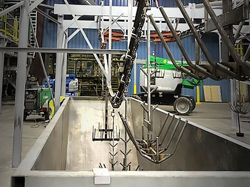 Overhead monorail system lowering metal parts into a dip tank at an industrial facility