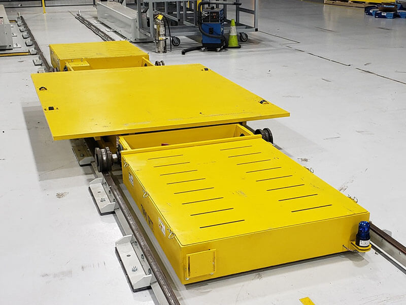 Yellow shuttle car on floor-mounted track for aerospace part transport, rated for 11,500 lb load capacity