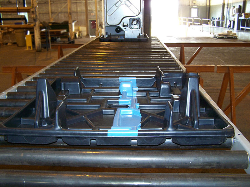 Plastic tray resting on gravity conveyor rollers in an industrial material handling system.