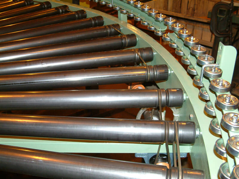 Close-up of grooved lineshaft conveyor rollers arranged in a curved frame for controlled accumulation.
