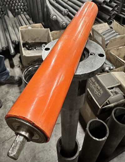 Roller with orange urethane sleeve for increased grip and product protection in conveyor systems.